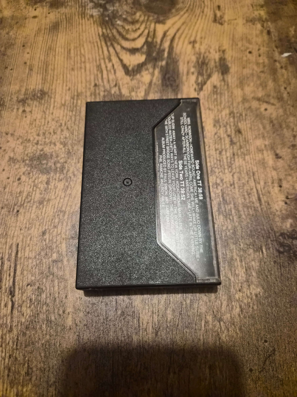 Simon and Garfunkel live concert cassette in a black case on a wooden surface.