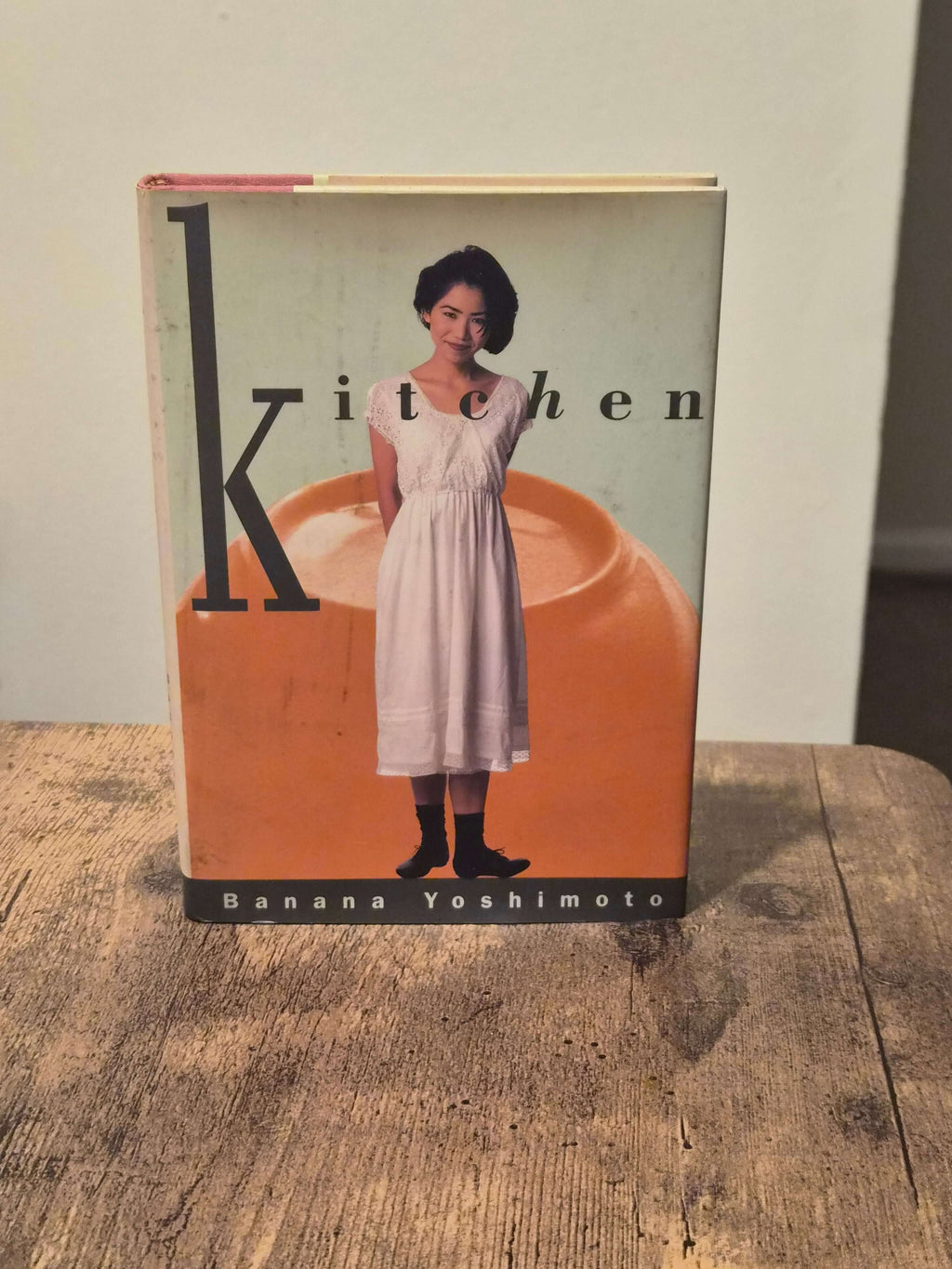 Banana Yoshimoto Kitchen first edition hardcover features a girl standing in front of an orange background.