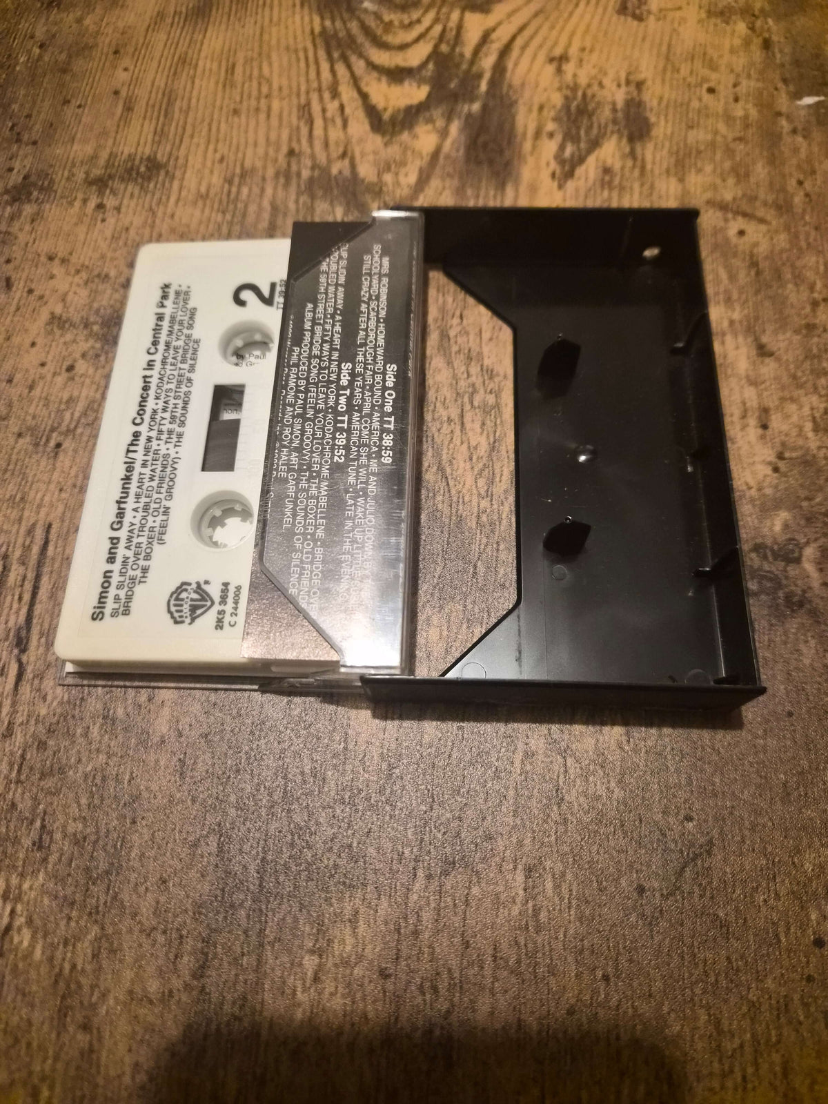 Simon and Garfunkel live concert cassette in cassette case on a wooden table surface.